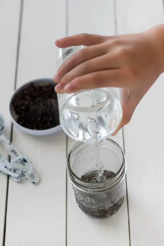 pouring water into a mason jar with one tablespoon of whole cloves