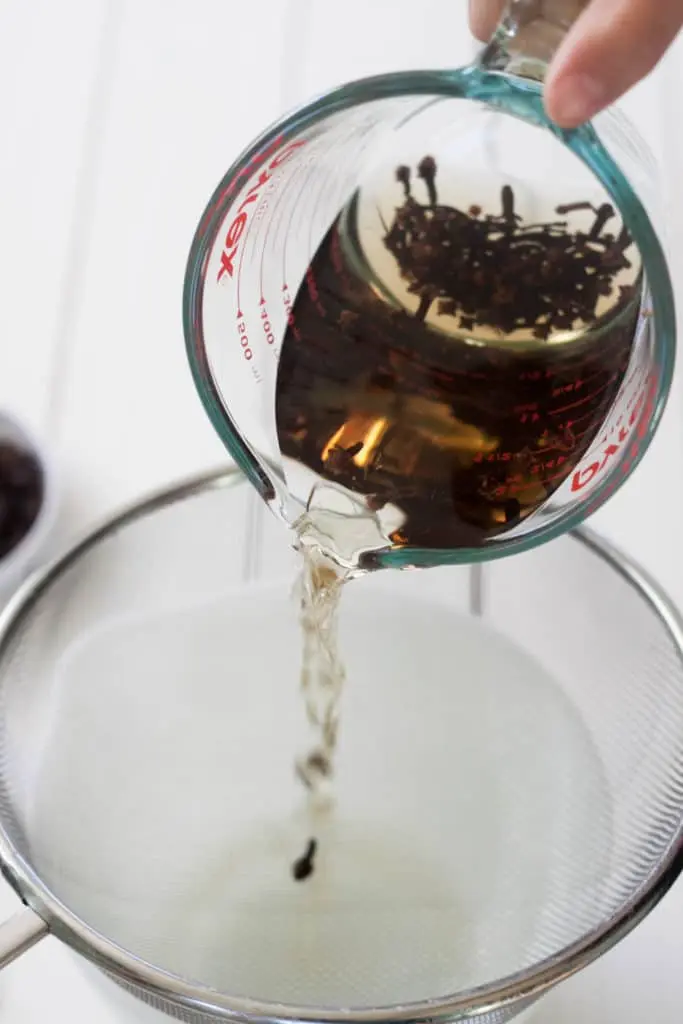 pouring whole cloves and water mixture into mesh strainer over glass bowl