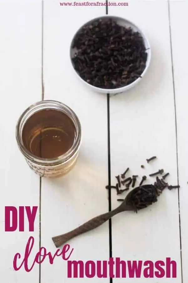 jar of DIY clove mouthwash, a wooden spoon of dried whole cloves and a bowl of whole cloves on white wooden background with title text