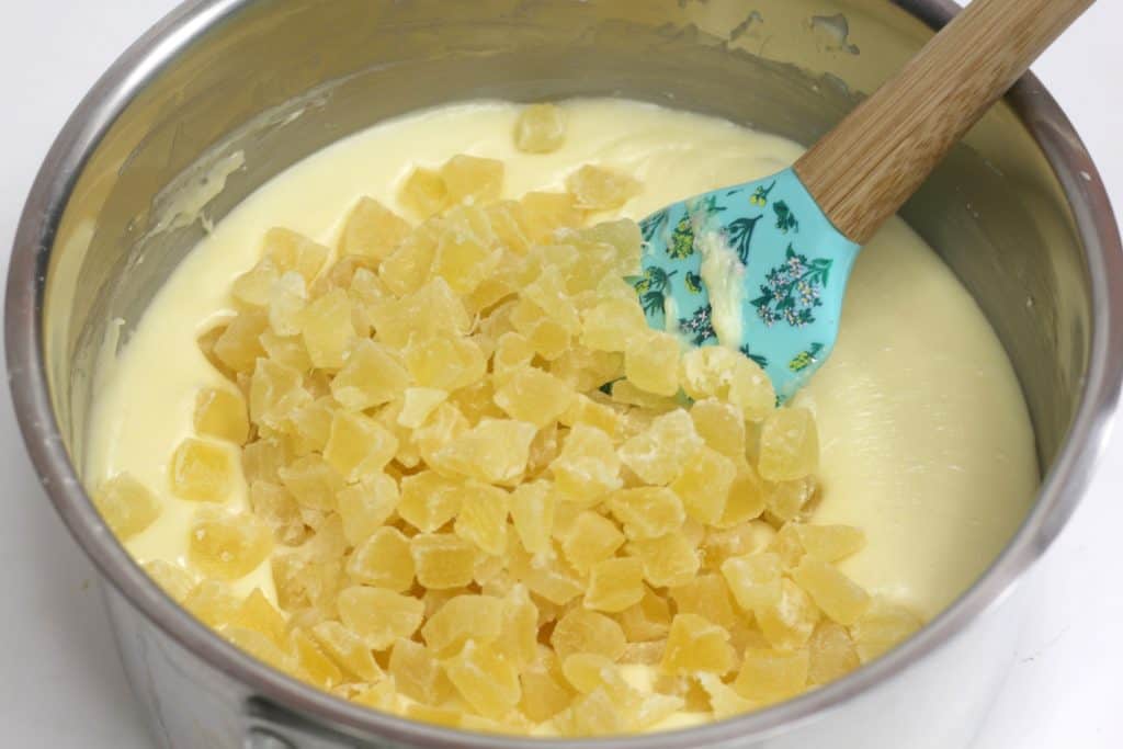 candied pineapple being mixed into melted white chocolate and sweetened condensed milk mixture in saucepan