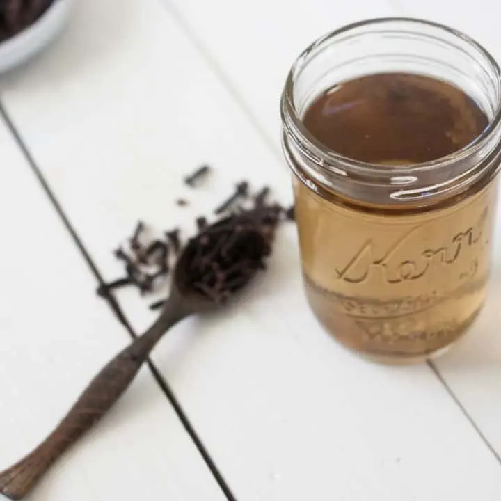 jar of clove mouthwash with wooden teaspoon of whole cloves