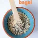 everything bagel seasoning in a teal bowl with a wooden spoon sitting on a white background