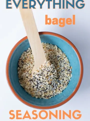 everything bagel seasoning in a teal bowl with a wooden spoon sitting on a white background
