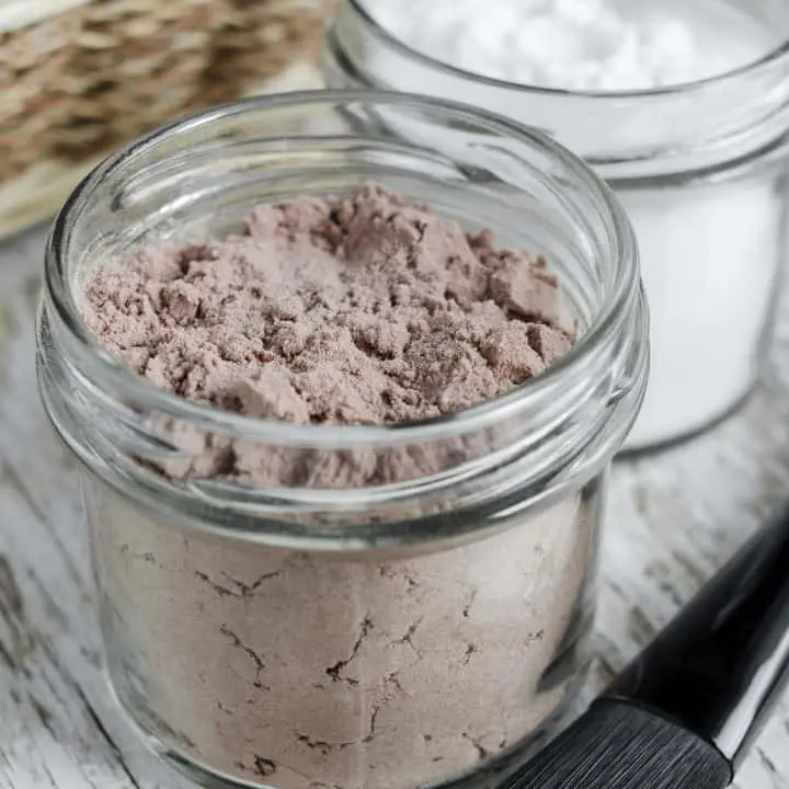 glass jar filled with dry shampoo powder sitting on wooden counter with makeup brush