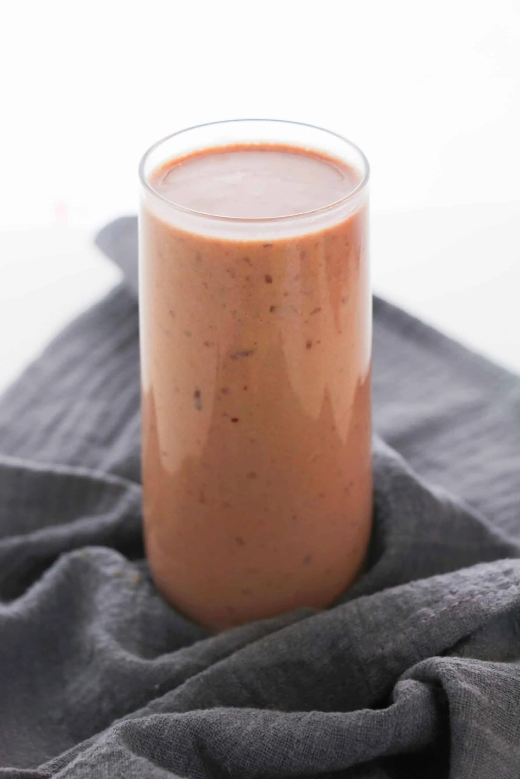 Cherry Banana smoothie in glass cup with gray cloth napkin on white surface