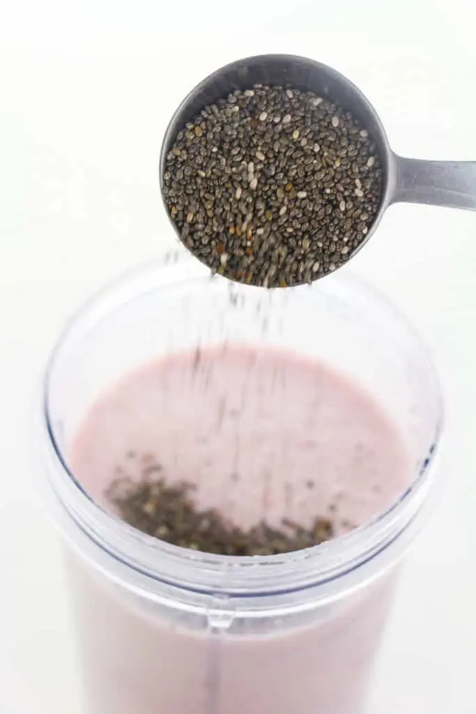 tablespoon of chia seeds poured into Cherry Banana smoothie in plastic blender cup