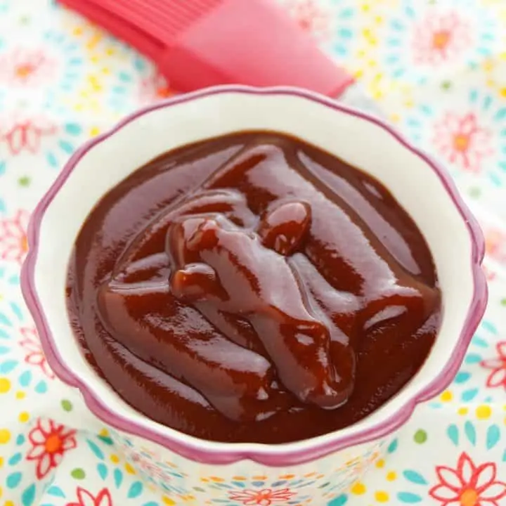 homemade bbq sauce in white bowl with red pastry brush on paisley tablecloth