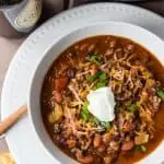 overhead of white bowl of chili on white plate with bottle of guinness beer and slow cooker