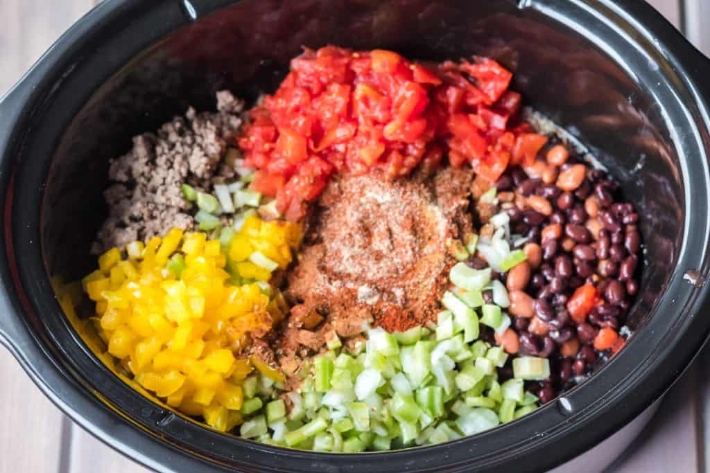 chopped peppers, black beans, ground beef, crushed tomatoes, and chopped celery in slow cooker