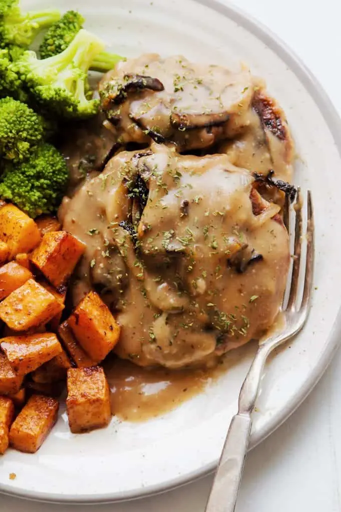 chicken Salisbury steak with mushroom and onion gravy on white plate with silver fork with steamed broccoli and roasted sweet potatoes