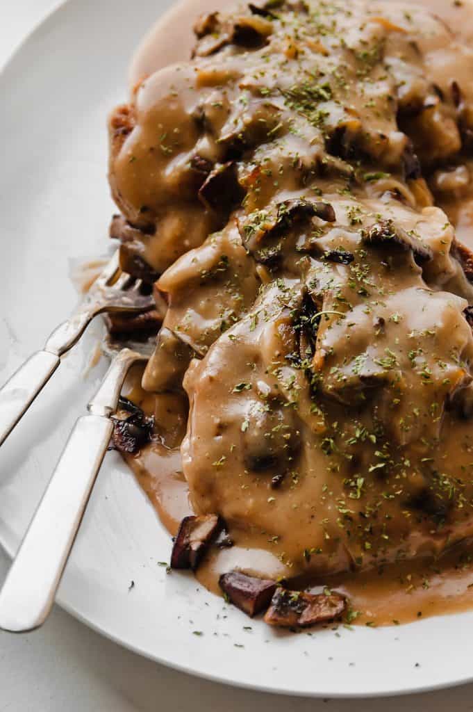 chicken Salisbury steak with mushroom and onion gravy on white platter with two silver forks