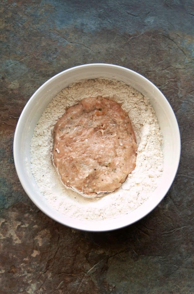chicken patty in bowl of flour on stone counter