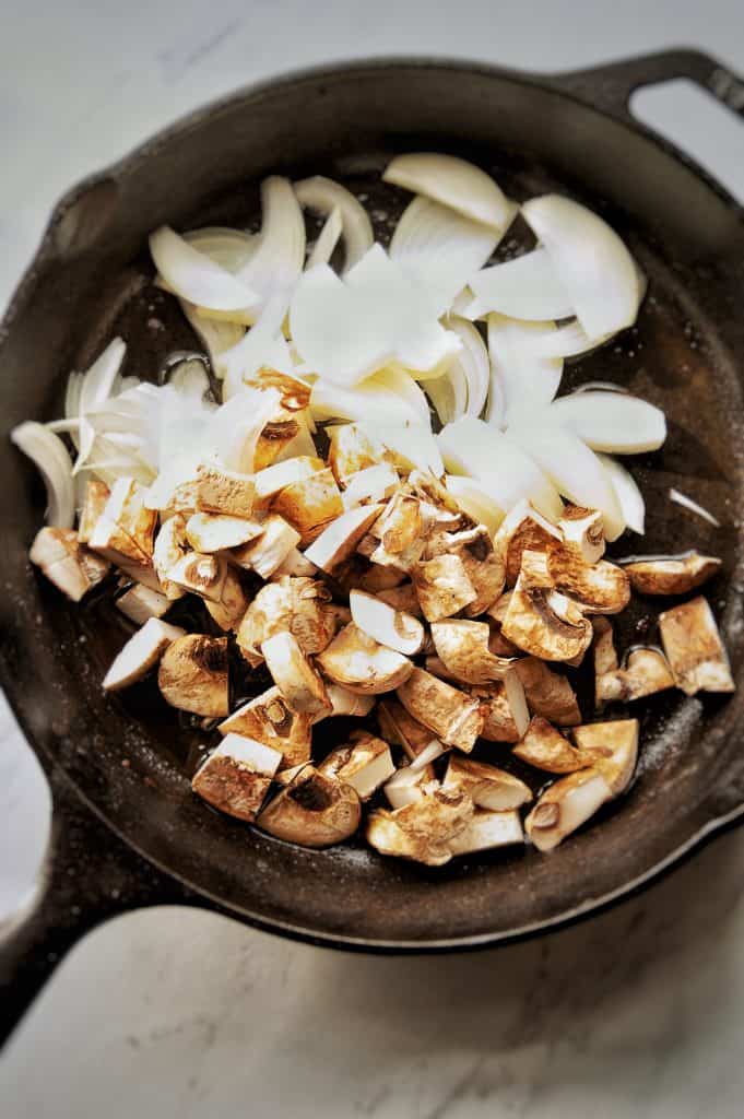 sliced onions and chopped mushrooms in cast iron skillet