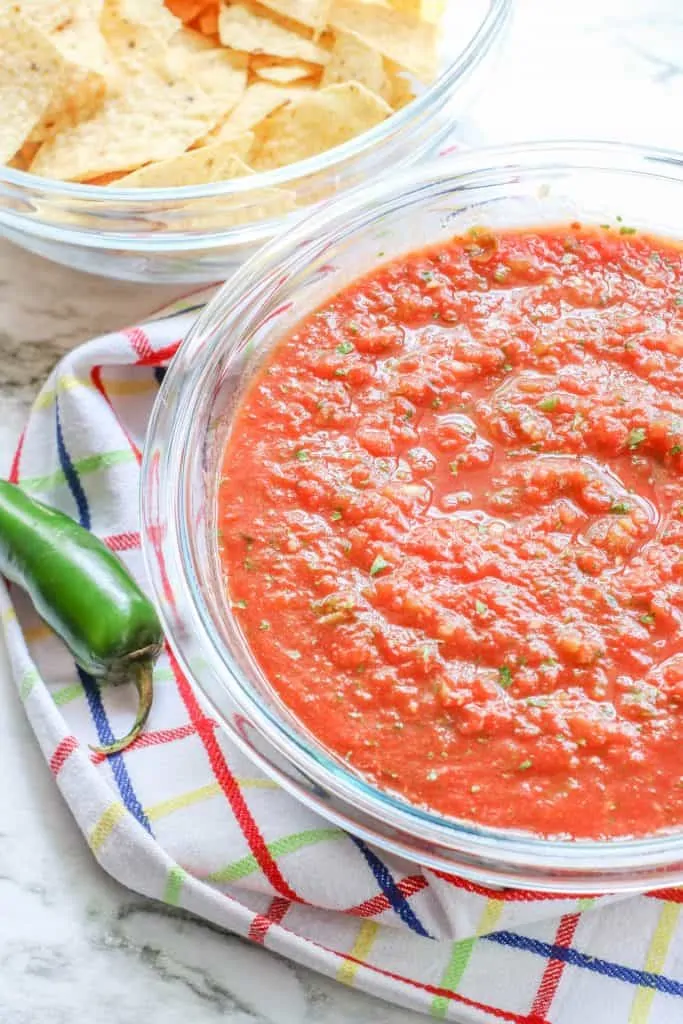 tortilla chips and homemade salsa in glass bowls on counter with jalapeno and towel