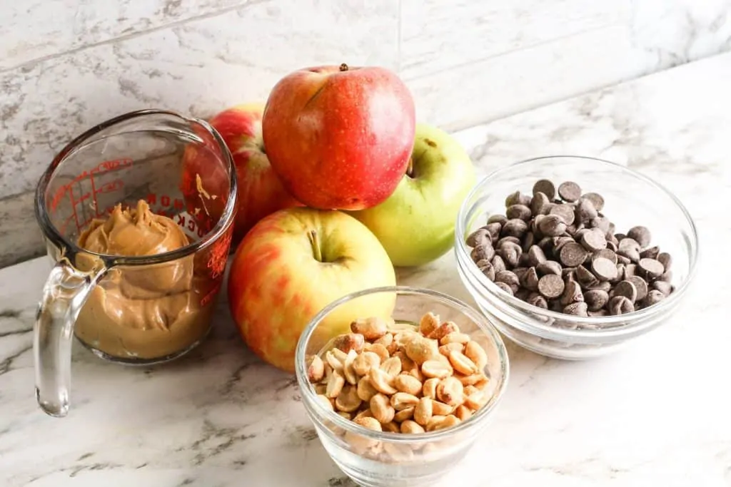 ingredients for apple nachos in glass bowls on marble counter