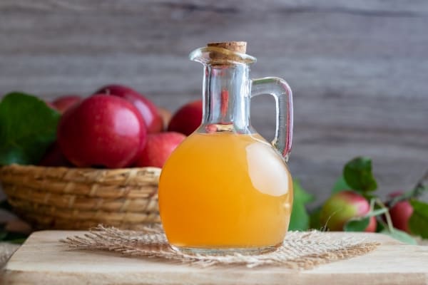 bottle of apple cider vinegar on wood board with bowl of apples