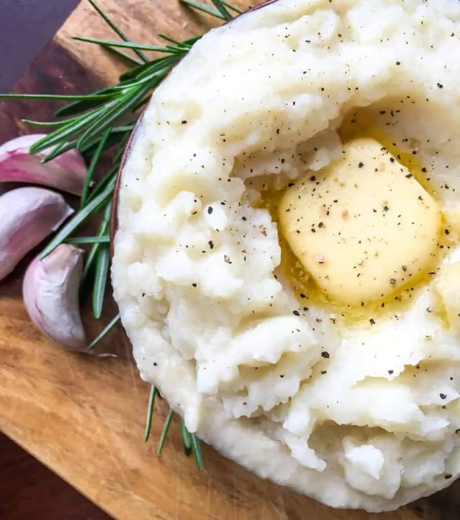 overhead of instant pot rosemary garlic mashed potatoes with garlic cloves and rosemary on cutting board