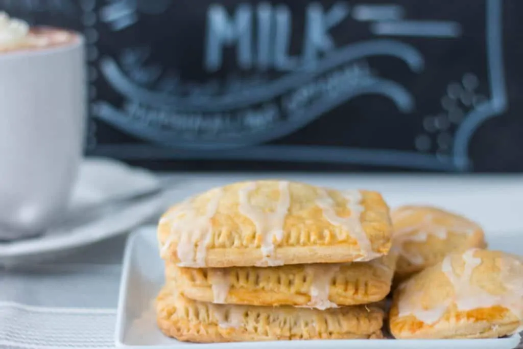 toaster pastries stacked on white square plate with cup of hot chocolate in background