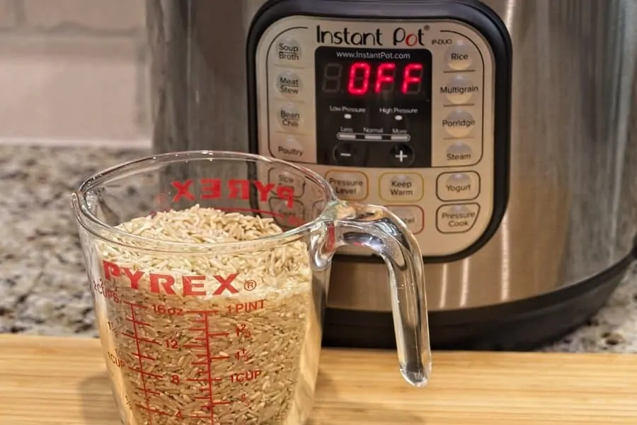 Instant Pot pressure cooker with glass measuring cup filled with brown rice sitting on wood cutting board