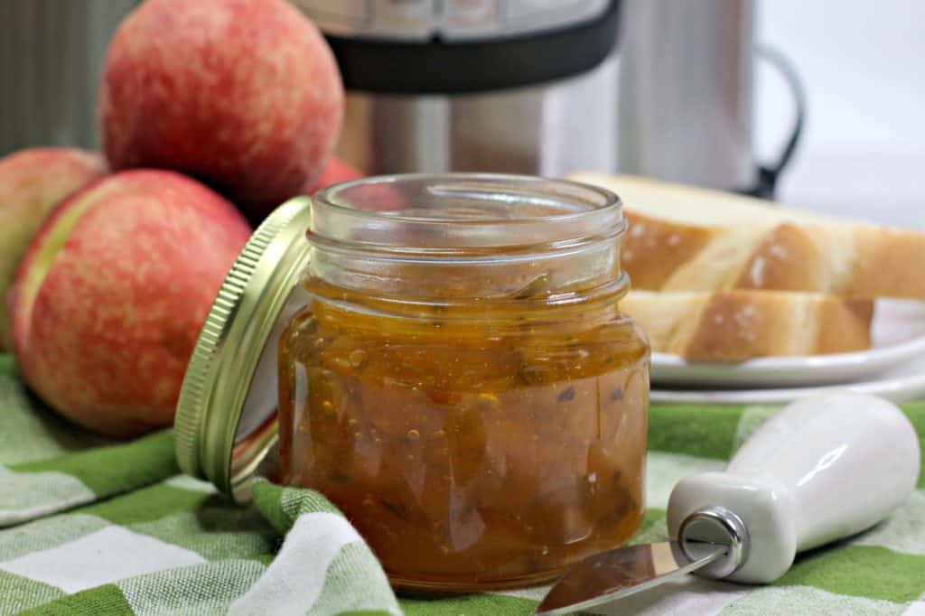 horizontal image of jar of peach jalapeno jam with spreader and slices of white bread