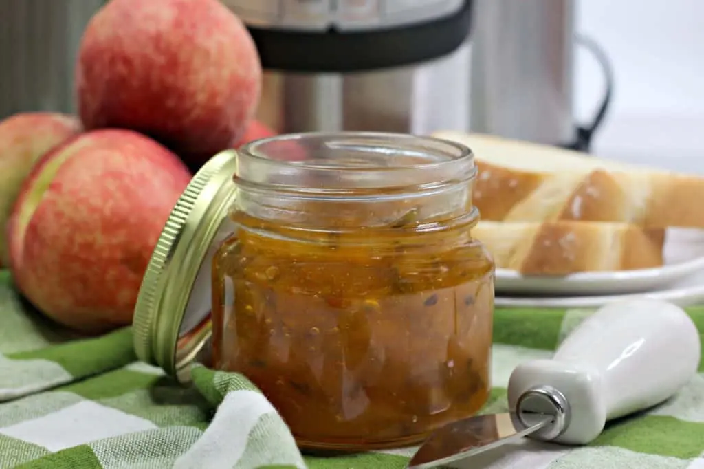 horizontal image of jar of peach jalapeno jam with spreader and slices of white bread