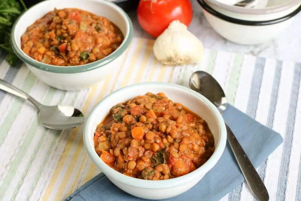 two bowls of lentil soup on striped placemat with garlic bulb and tomato