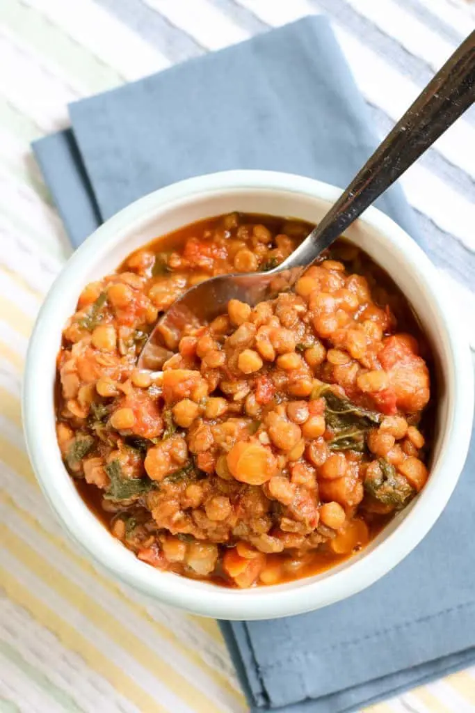 overhead view of lentil soup in white bowl with blue napkin