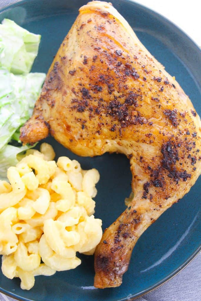 baked chicken leg quarter on blue plate with macaroni and cheese and salad