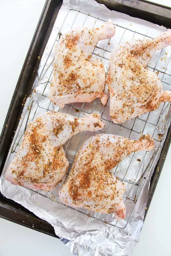 uncooked chicken leg quarters seasoned on a baking sheet