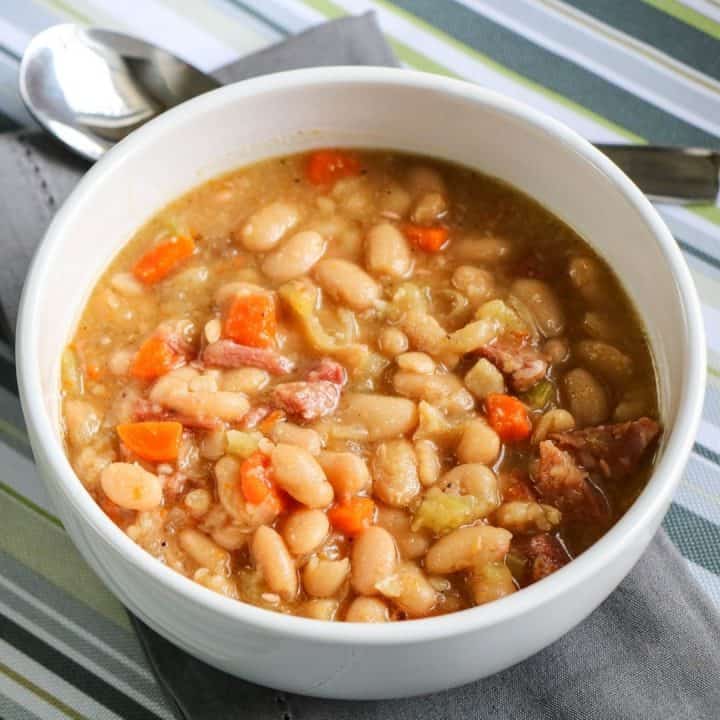 crock pot ham and bean soup in white bowl on striped tablecloth