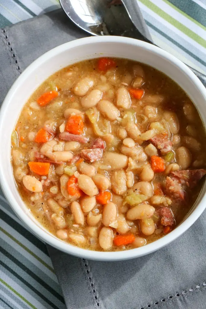 overhead of ham and bean soup in white bowl with gray napkin and spoon