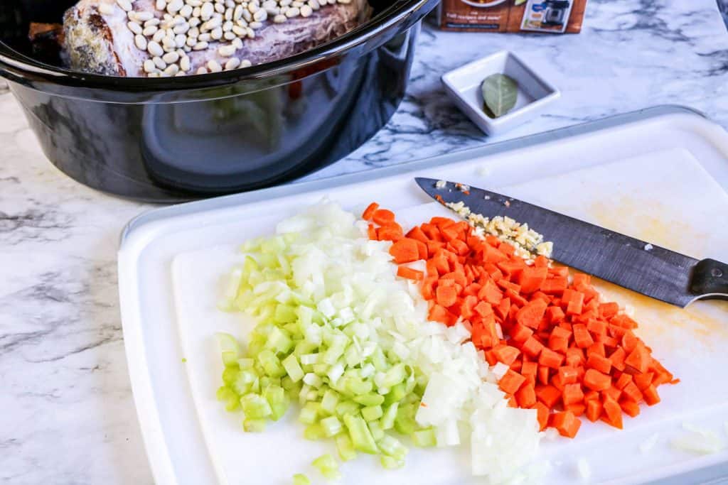diced celery, onion and carrots on cutting board with knife