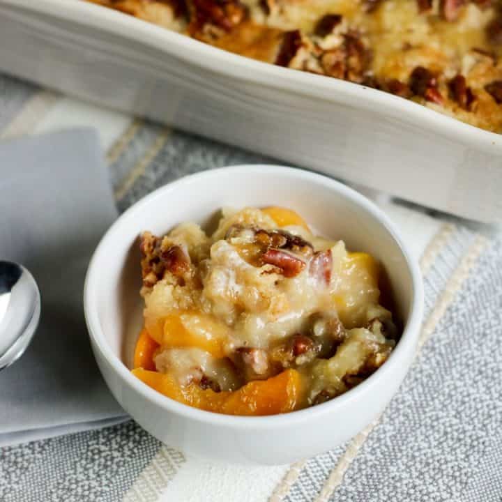 square image of white chocolate peach dump cake in white bowl with blue napkin