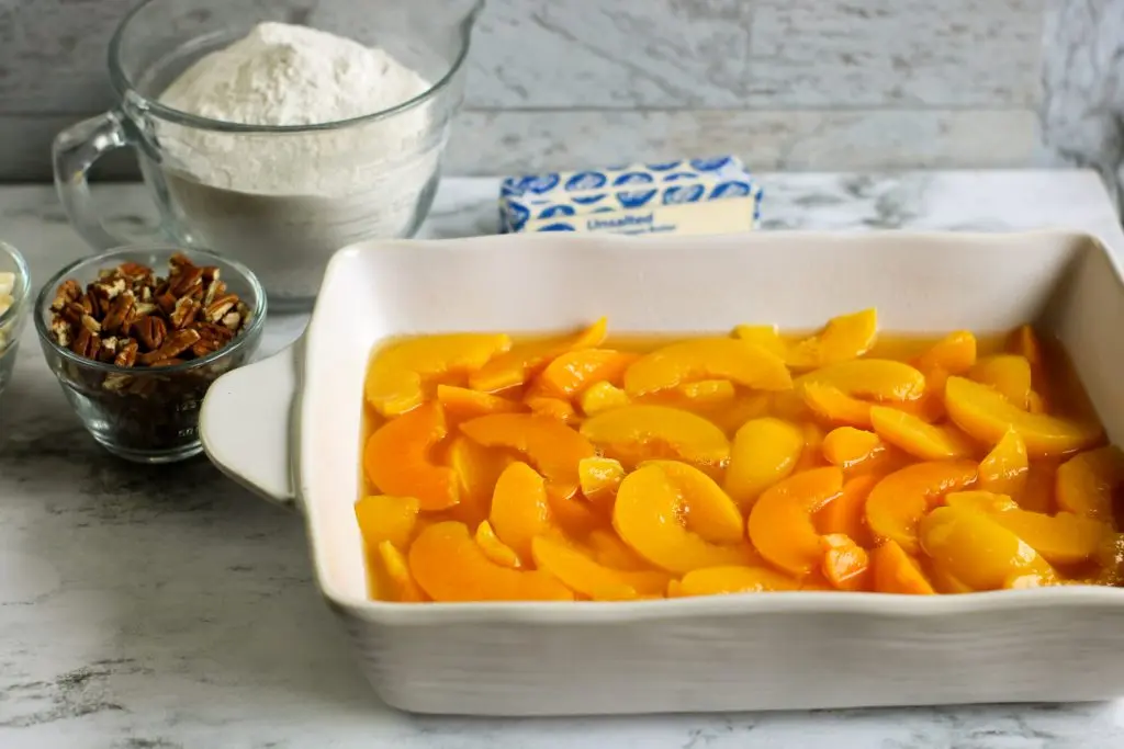 canned peaches in white baking dish with white chocolate peach dump cake ingredients