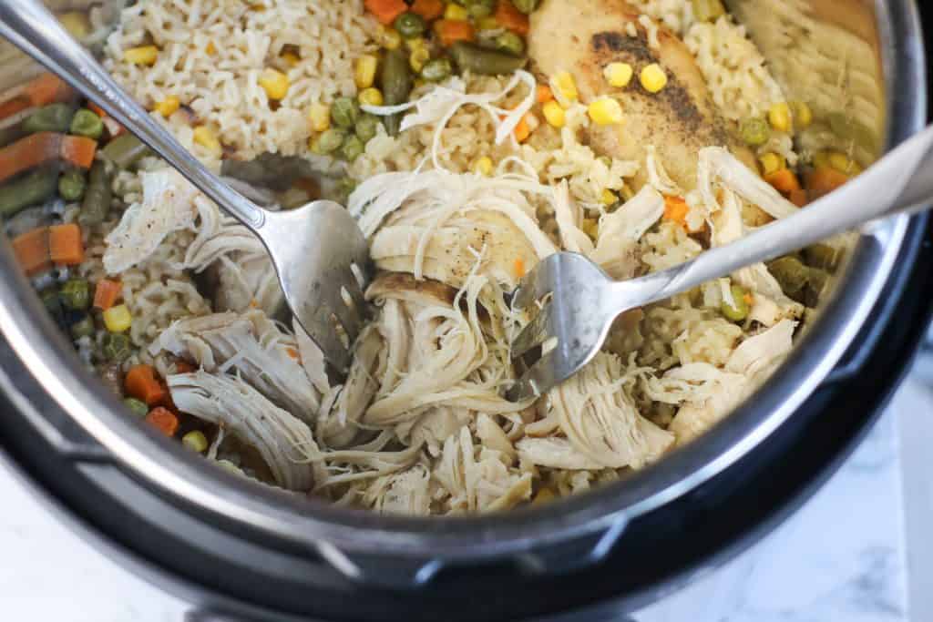 two forks shredding chicken breast in instant pot with rice and vegetables