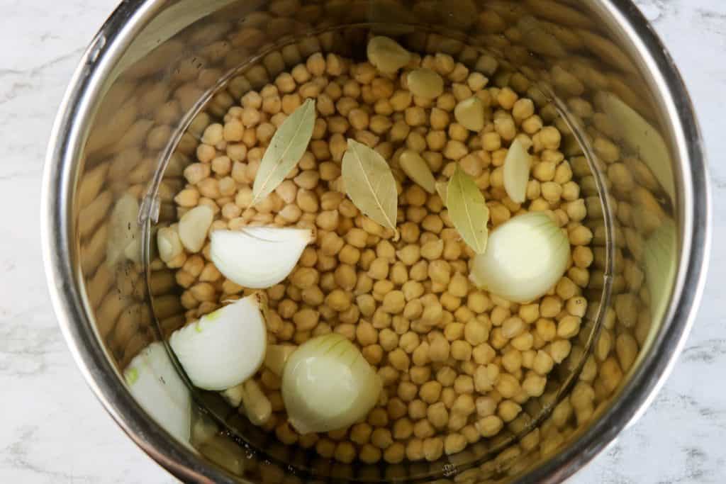 overhead view of dried chickpeas, water, garlic, onion and bay leaves in instant pot