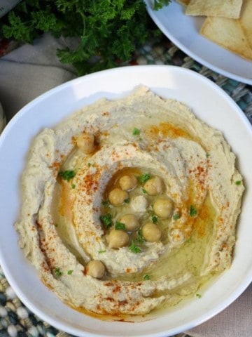 overhead of instant pot hummus in white bowl with chopped parsley and pita chips