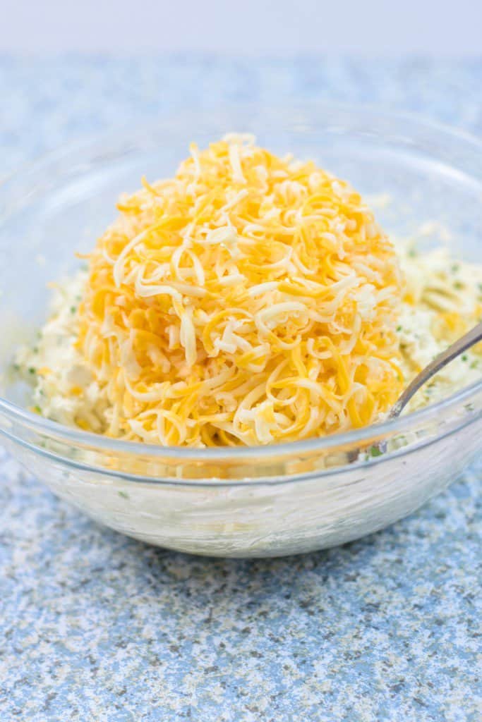 A bowl of shredded cheese with a spoon in it, perfect for an everything bagel cheese ball recipe.
