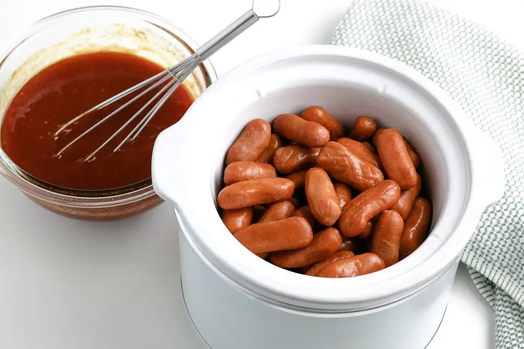 little smokies in crockpot and bbq sauce in glass bowl with whisk