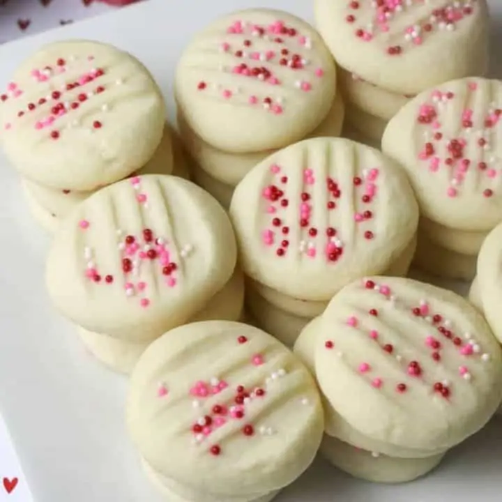 square closeup of whipped shortbread cookies stacked on white plate