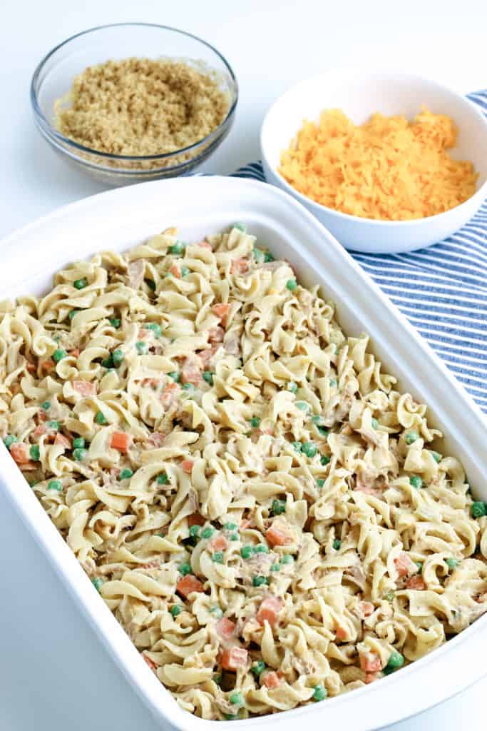 unbaked tuna noodle casserole in baking dish with breadcrumbs and shredded cheese