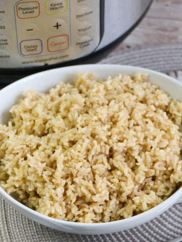 brown rice in round white bowl with instant pot in background on gray placemat