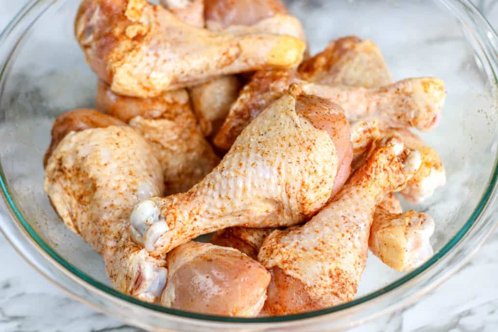 chicken legs in glass bowl seasoned with spices