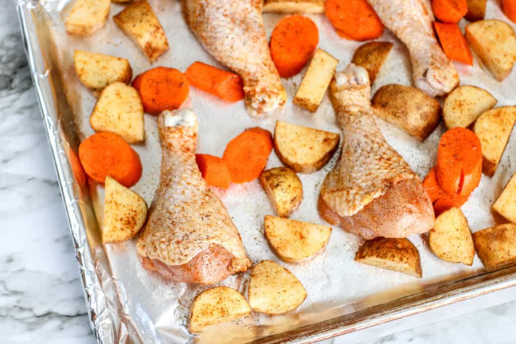 unbaked chicken drumsticks and cut carrots and potatoes on sheet pan