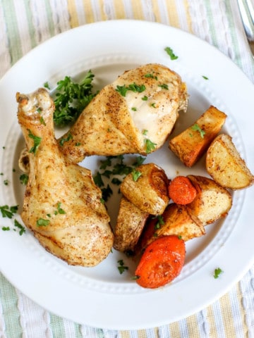 two chicken drumsticks and roasted carrots and potatoes on white plate with pastel tableclock