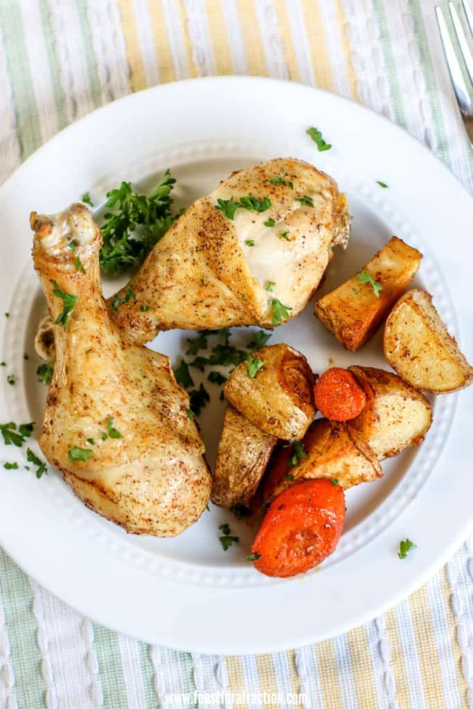 two chicken drumsticks and roasted carrots and potatoes on white plate with pastel tableclock