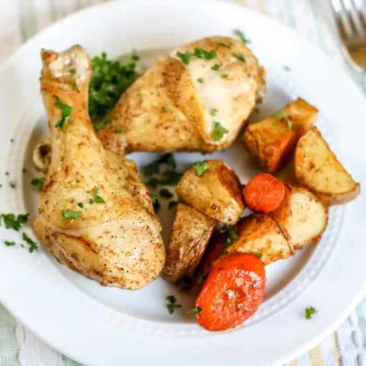 baked chicken drumsticks and potatoes and carrots on white plate with fork