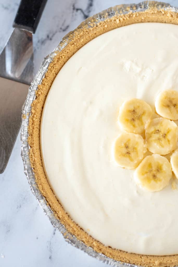 overhead view of whole banana pudding pie with sliced bananas on top with metal spatula