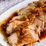 slices of slow cooked pork loin roast on white plate with onions and sauce