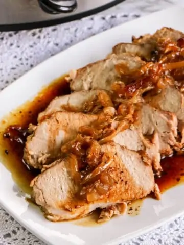 slices of slow cooked pork loin roast on white plate with onions and sauce